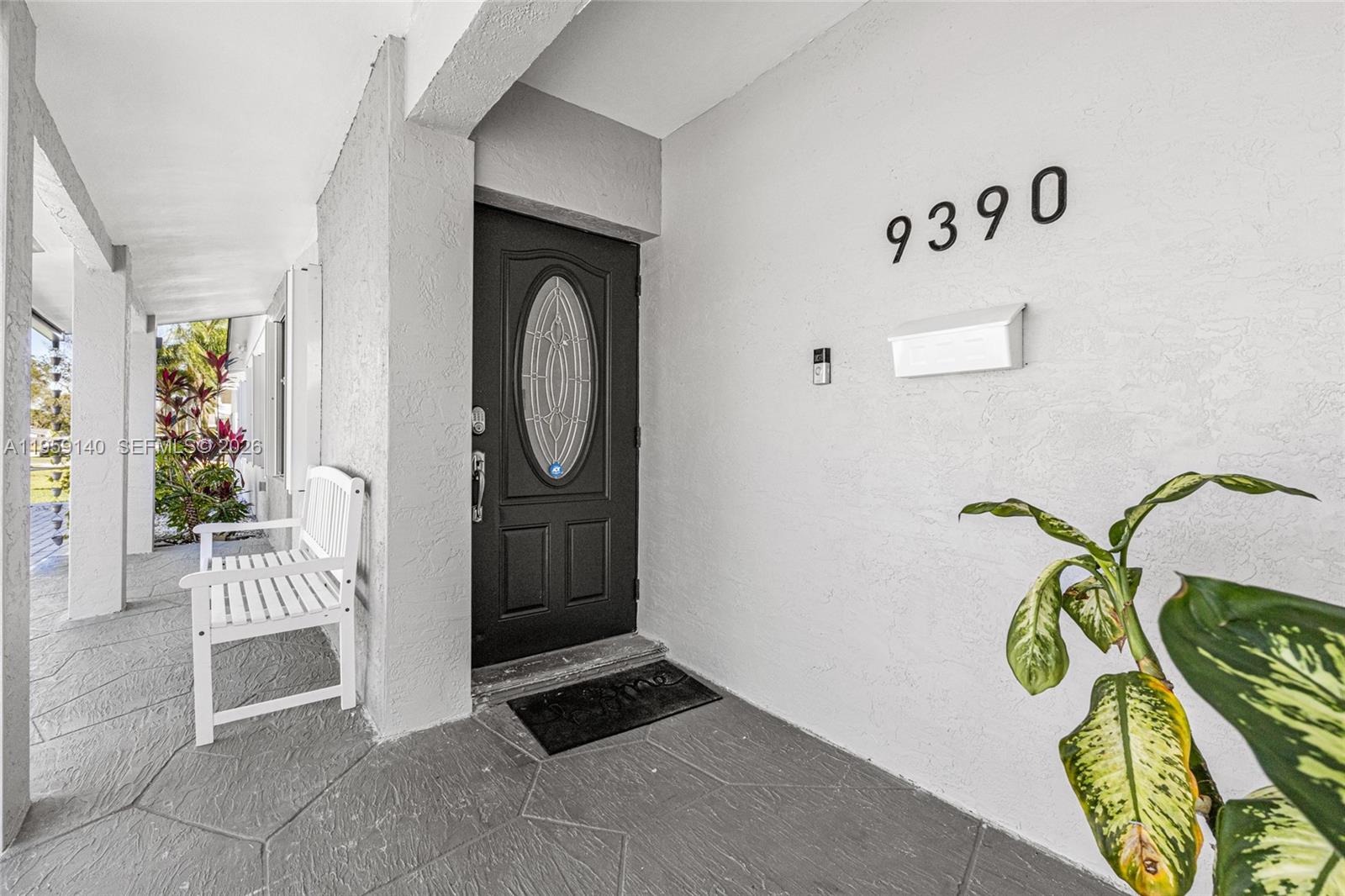 A covered porch features a black front door, a white bench, and a potted plant — 9390 SW 190th St, Cutler Bay FL 33157, CUTLER BAY, FL