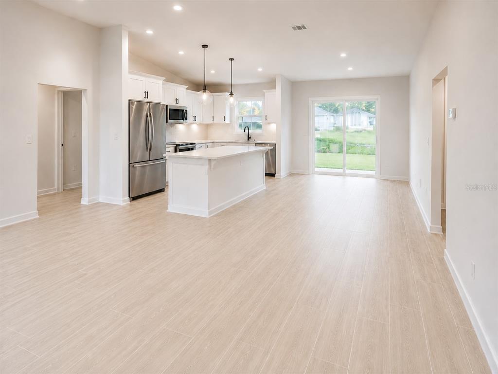 A modern kitchen features white cabinetry, stainless steel appliances, a center island, and light flooring — 11081 SW 107TH PLACE, OCALA, FL