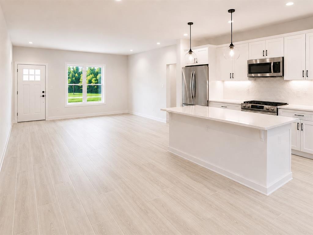 A modern kitchen with white cabinets and a quartz island opens into a spacious living area — 11081 SW 107TH PLACE, OCALA, FL