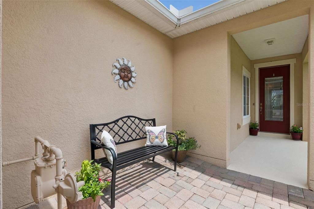 A paved entryway features a black metal bench, a sun wall decoration, and a red door — 1381 ABBOT WAY, DELAND, FL