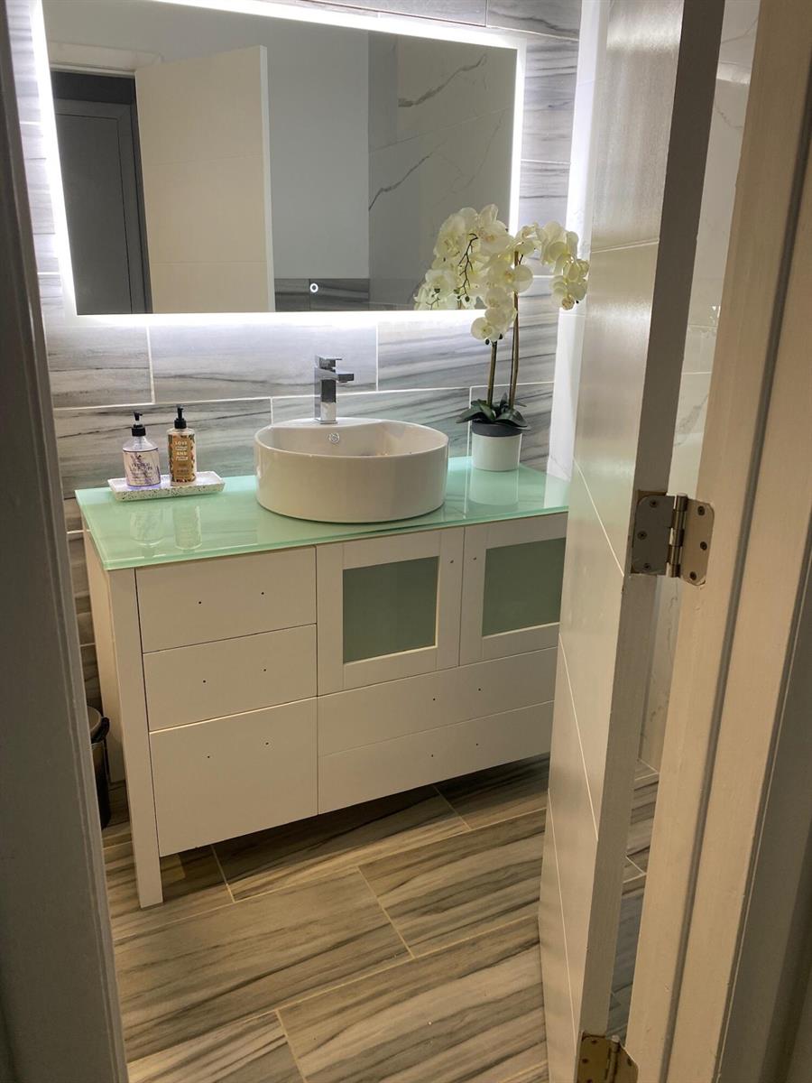 A modern bathroom features a white vessel sink, glass countertop, and a backlit wall mirror — 7913 Kismet Street, Miramar FL 33023, MIRAMAR, FL