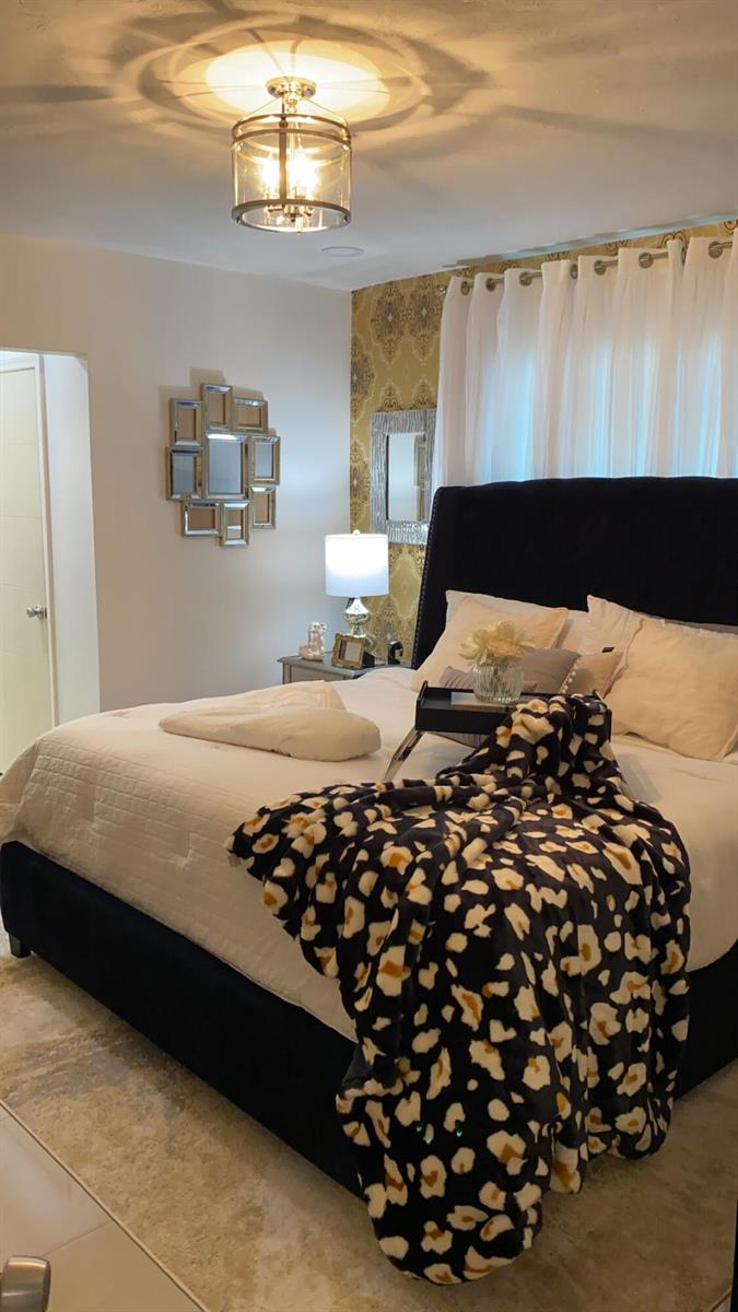 A bedroom features a dark upholstered bed, patterned wallpaper, a chandelier, and a leopard-print throw — 7913 Kismet Street, Miramar FL 33023, MIRAMAR, FL