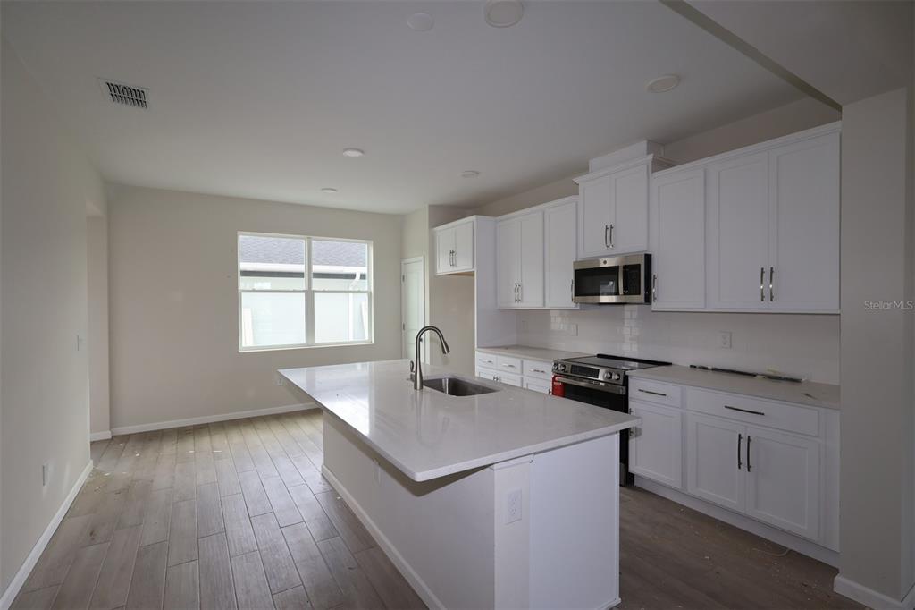 A kitchen features a white island with a sink, light wood flooring, and recessed lighting — 1417 HYDE STREET, ST CLOUD, FL