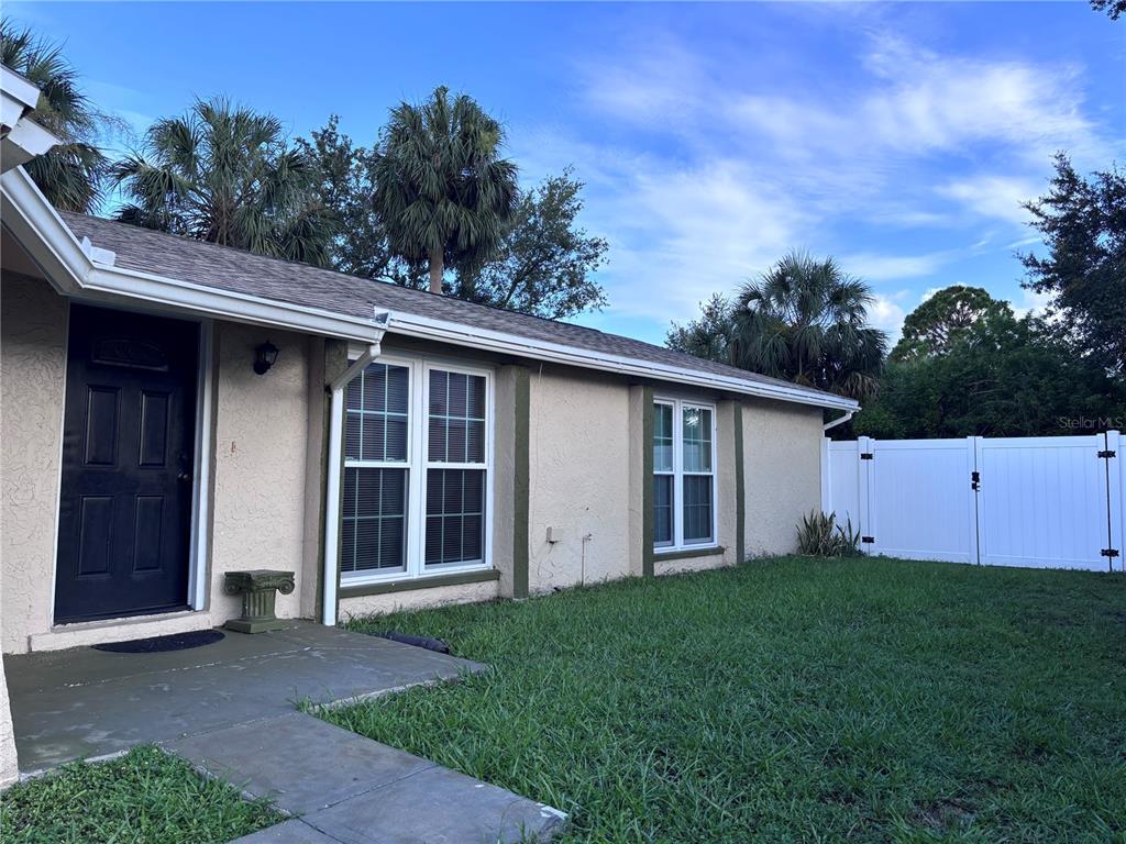 A tan house exterior features a black front door, two windows, and a white fence — 10102 MISSY COURT, TAMPA, FL