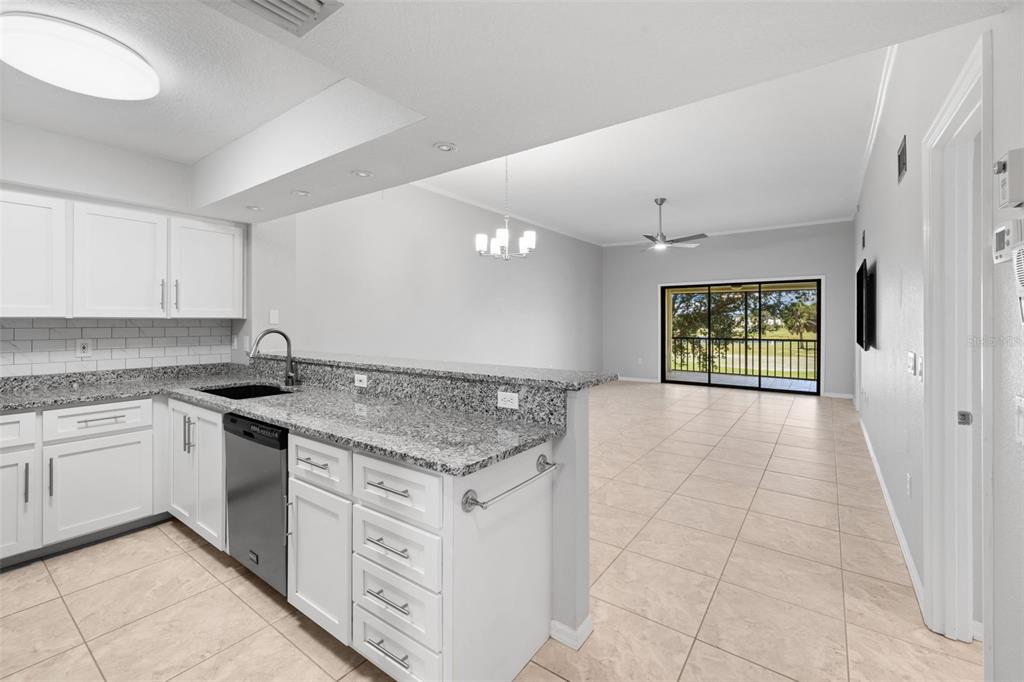 A kitchen with white cabinets and granite countertops overlooks an open living area with tile — 1335 SAXONY CIRCLE UNIT 324, PUNTA GORDA, FL