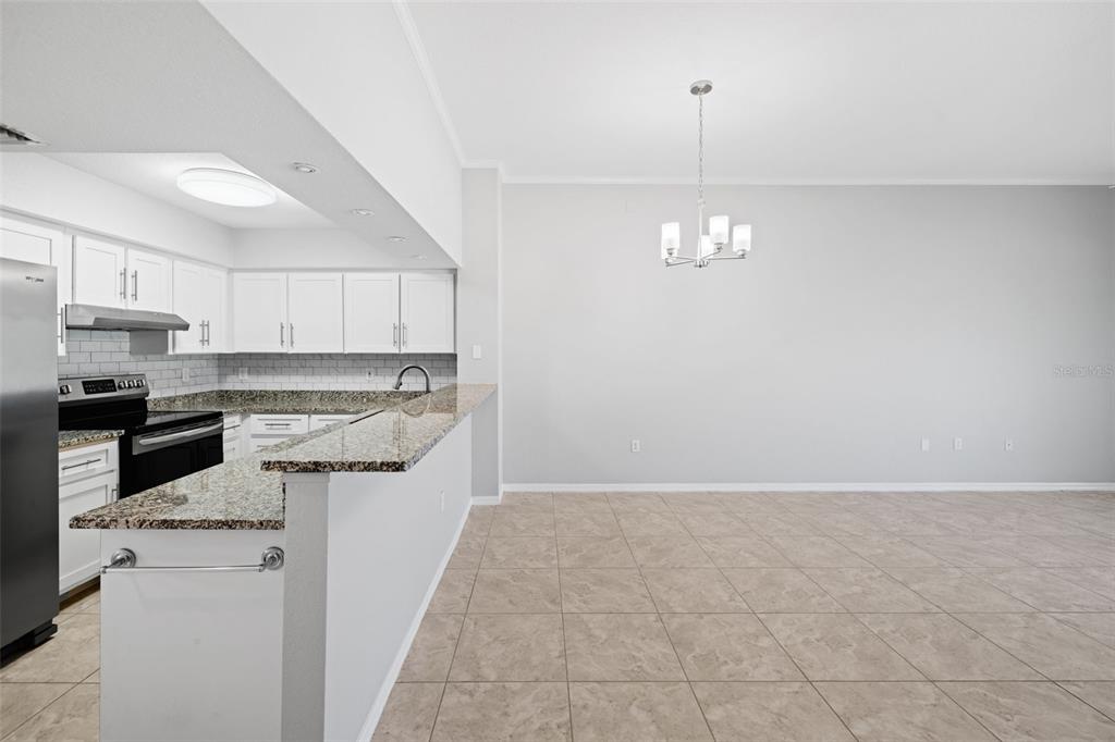 A kitchen with granite countertops and white cabinets opens to a dining area with tile — 1335 SAXONY CIRCLE UNIT 324, PUNTA GORDA, FL