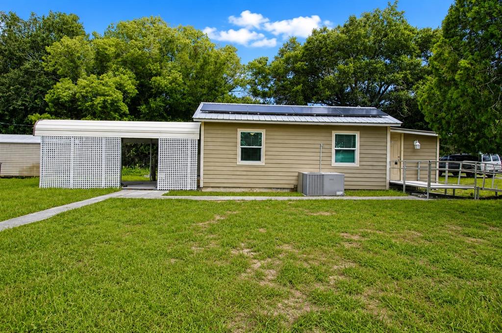 A tan house with a white carport, solar panels, and a metal wheelchair ramp — 5811 11TH STREET, ZEPHYRHILLS, FL