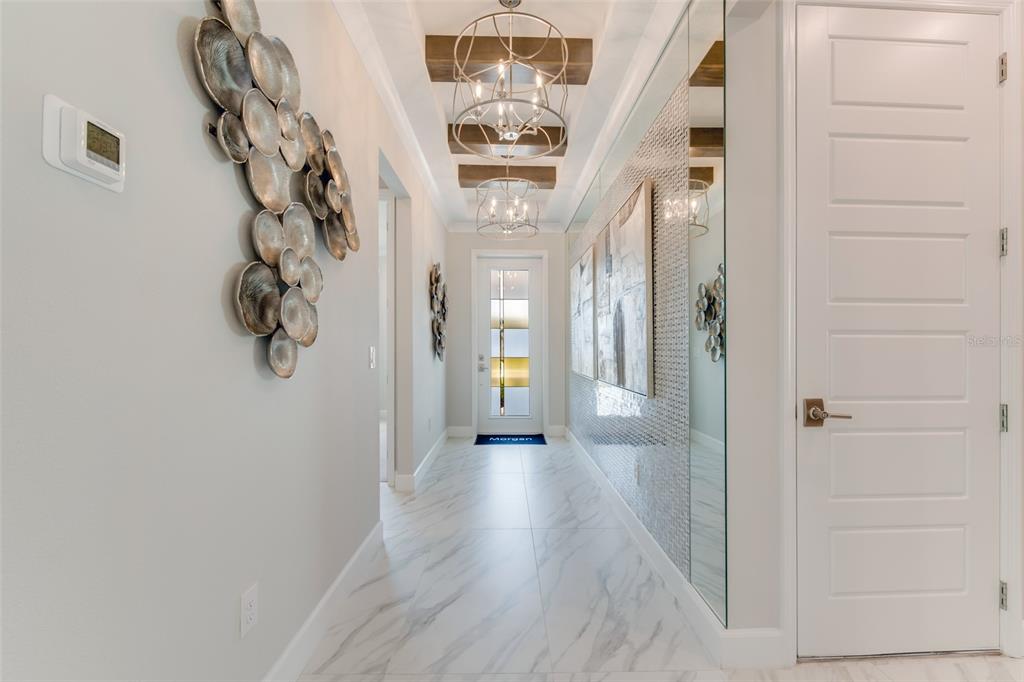 A bright hallway features marble-look tile floors, mirrored walls, decorative metal wall art, and chandeliers — 1193 CRESSWIND BOULEVARD, DELAND, FL
