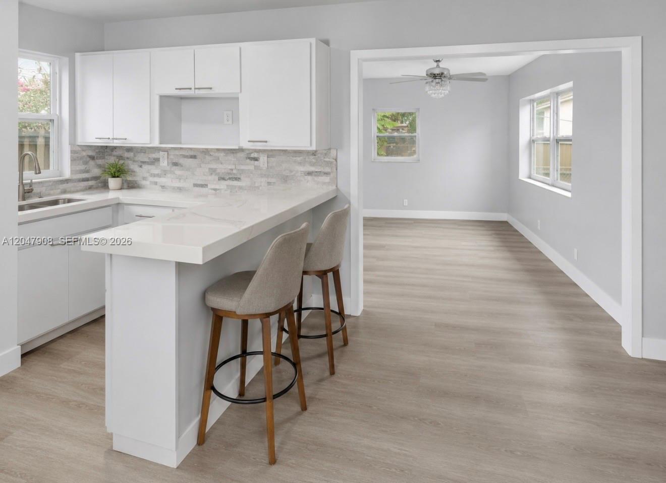 A kitchen with white cabinets and a breakfast bar opens into a light-filled dining area — 432 NW 103rd St # 2, Miami FL 33150, MIAMI, FL