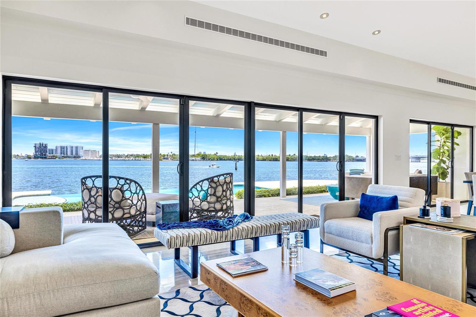 A living room with floor-to-ceiling sliding glass doors overlooking a waterfront patio and pool — 1290 NE 83rd Street, Miami FL 33138, MIAMI, FL