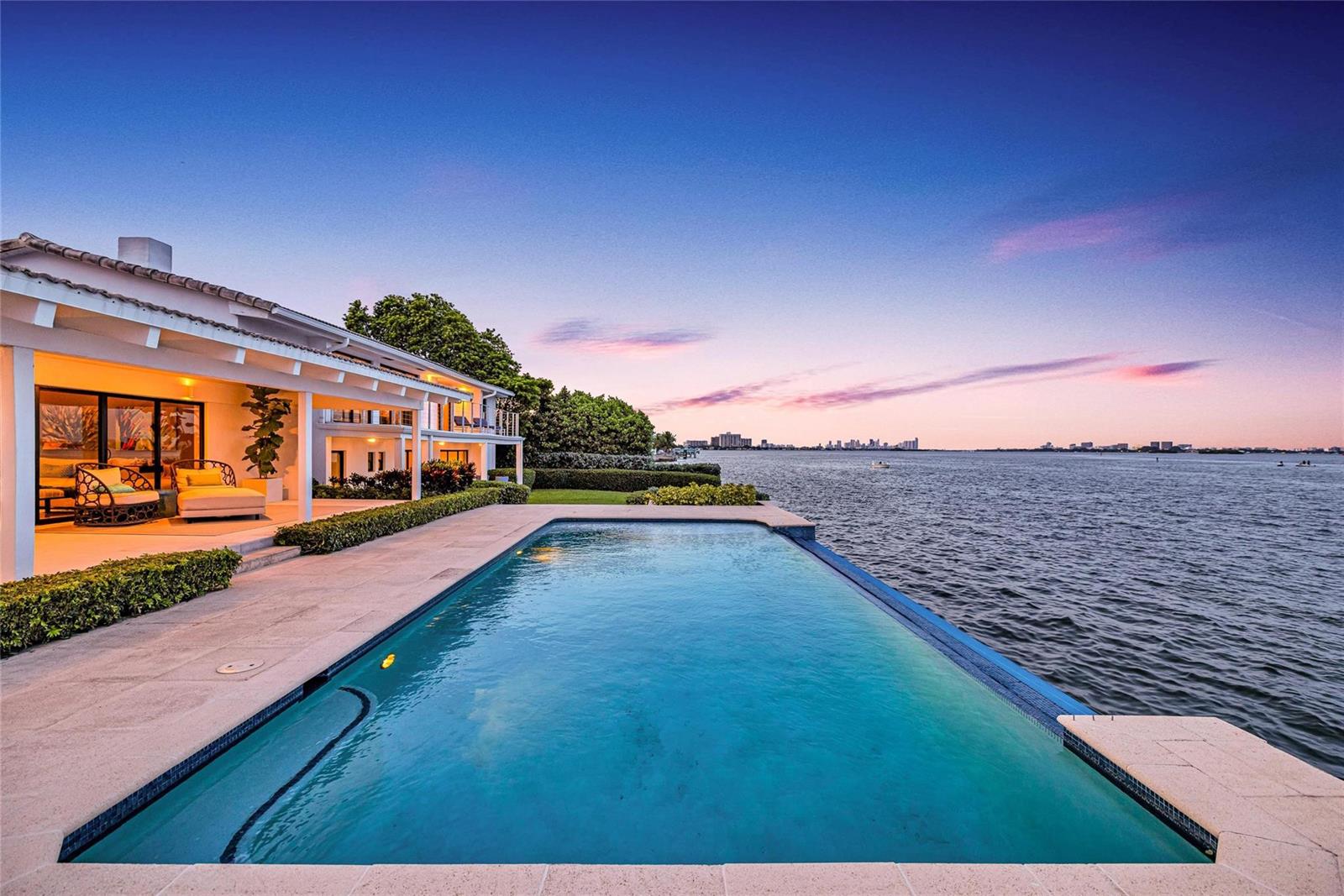 An infinity pool overlooks a large body of water at sunset next to a modern house — 1290 NE 83rd Street, Miami FL 33138, MIAMI, FL