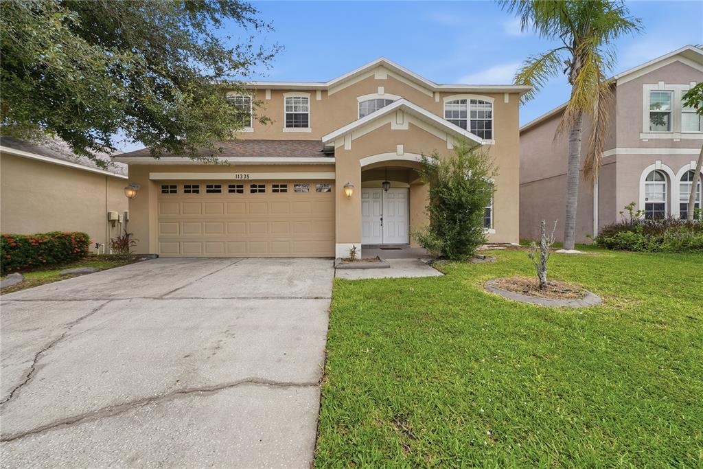 A two-story tan suburban house with a two-car garage and a concrete driveway — 11335 VILLAGE BROOK DRIVE, RIVERVIEW, FL