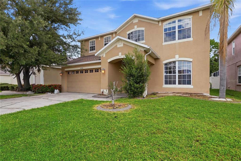 A two-story tan stucco house with a two-car garage and a front lawn — 11335 VILLAGE BROOK DRIVE, RIVERVIEW, FL