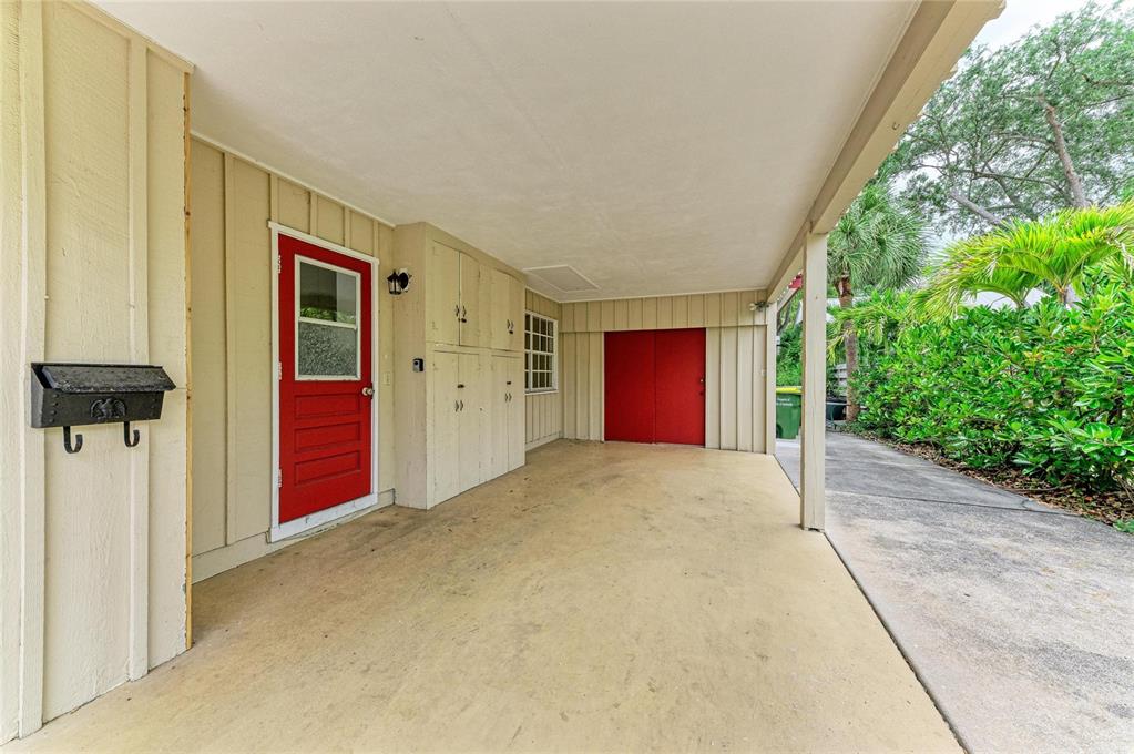 A covered carport features a red door, storage cabinets, and a concrete floor — 1827 ALTA VISTA STREET, SARASOTA, FL