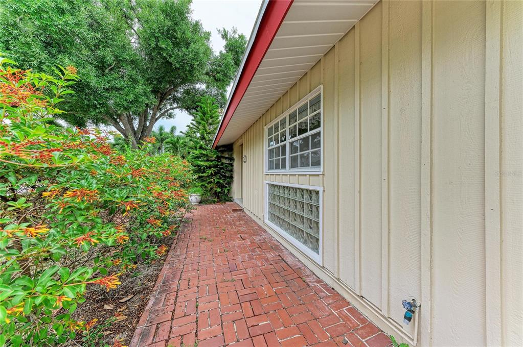 A brick walkway runs alongside a beige house with a glass block window and siding — 1827 ALTA VISTA STREET, SARASOTA, FL