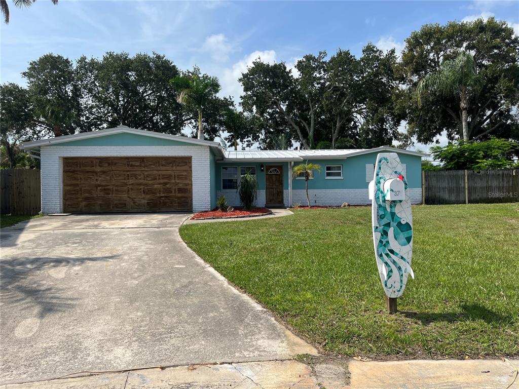 A single-story house with a teal exterior, white brick accents, and a surfboard-shaped mailbox — 375 CARROUSEL COURT, MERRITT ISLAND, FL
