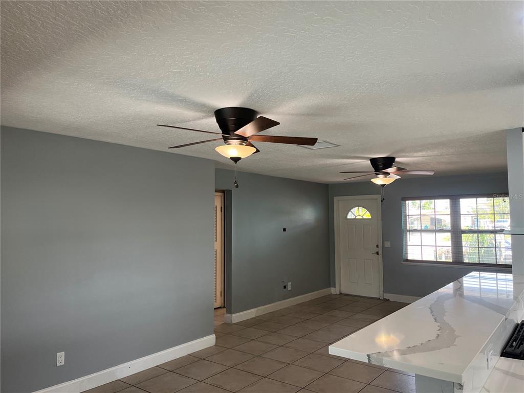 A room with gray walls, tiled floors, two ceiling fans, and a white kitchen counter — 375 CARROUSEL COURT, MERRITT ISLAND, FL