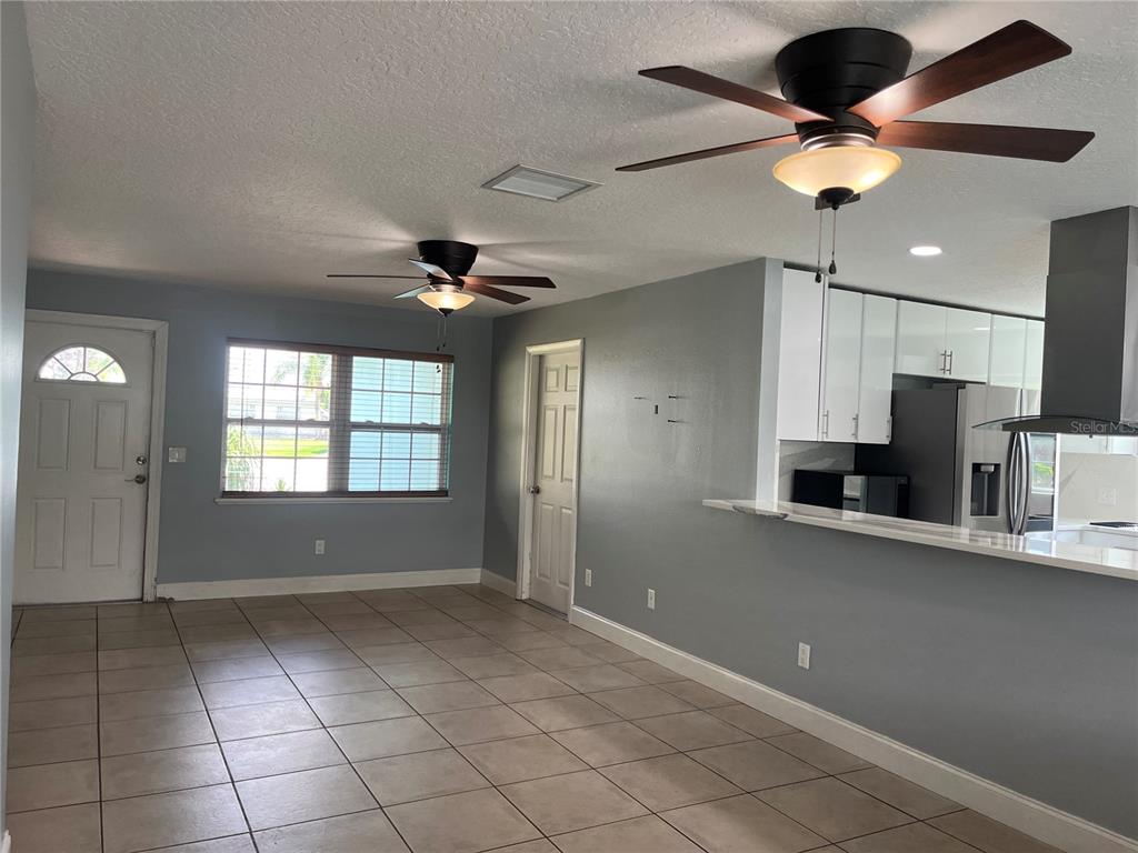 An open-concept room features light gray walls, tile flooring, two ceiling fans, and a kitchen — 375 CARROUSEL COURT, MERRITT ISLAND, FL