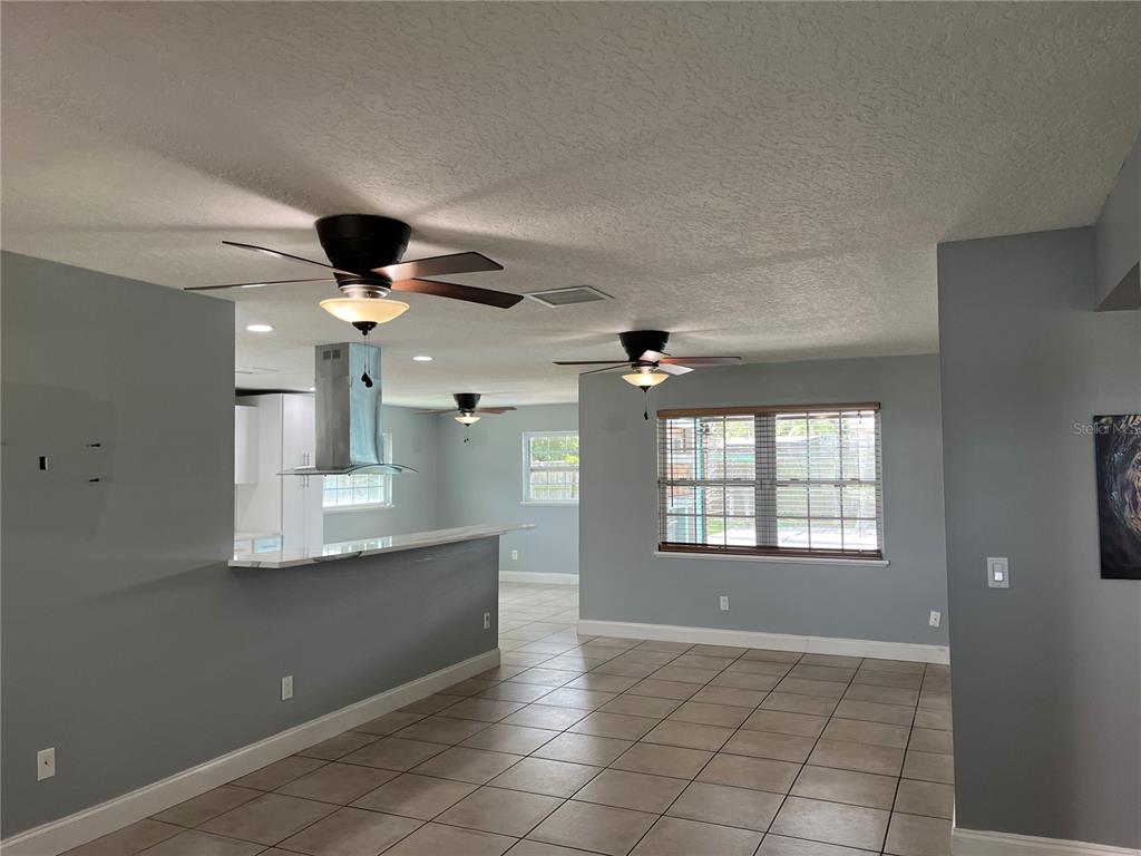 An open-concept living area features light gray walls, tile flooring, and multiple ceiling fans — 375 CARROUSEL COURT, MERRITT ISLAND, FL