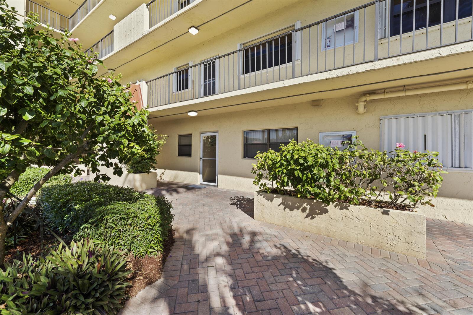 A paved walkway leads to a building entrance flanked by landscaped planters and green shrubs — 7420 S Ocean Drive # 113, Jensen Beach FL 34957, JENSEN BEACH, FL