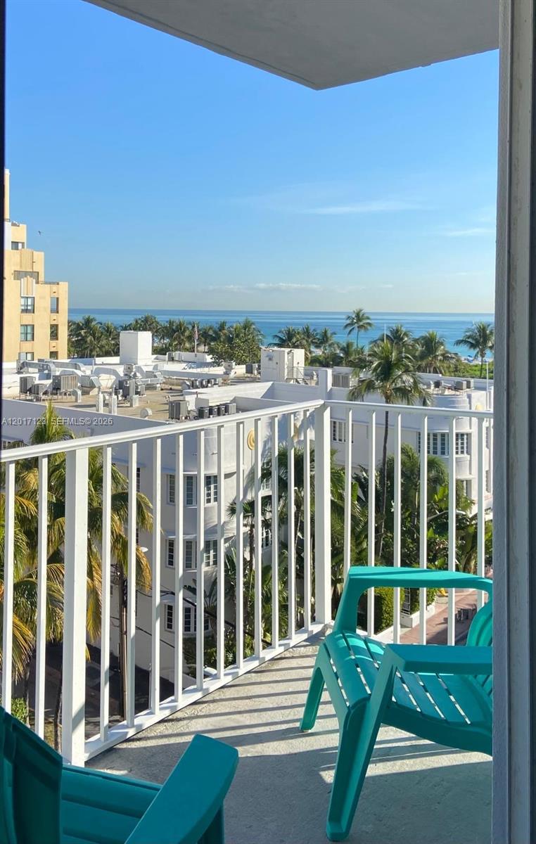 A balcony with two teal chairs overlooks a white building and the ocean — MIAMI BEACH, FL