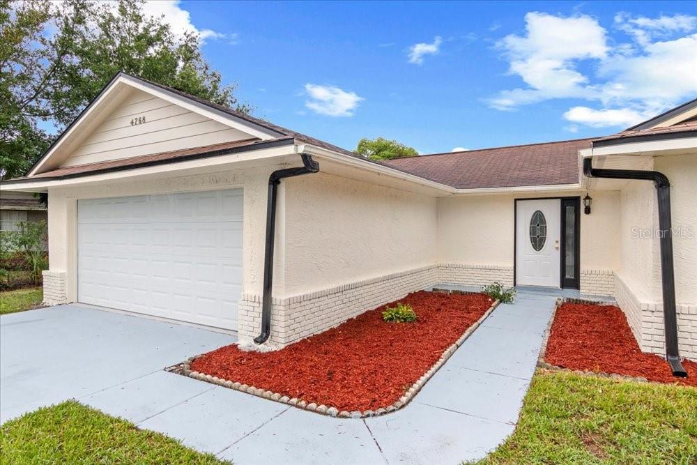 A single-story house features a white stucco exterior, a two-car garage, and red mulch landscaping — 4768 CROSSBOW COURT, ORLANDO, FL