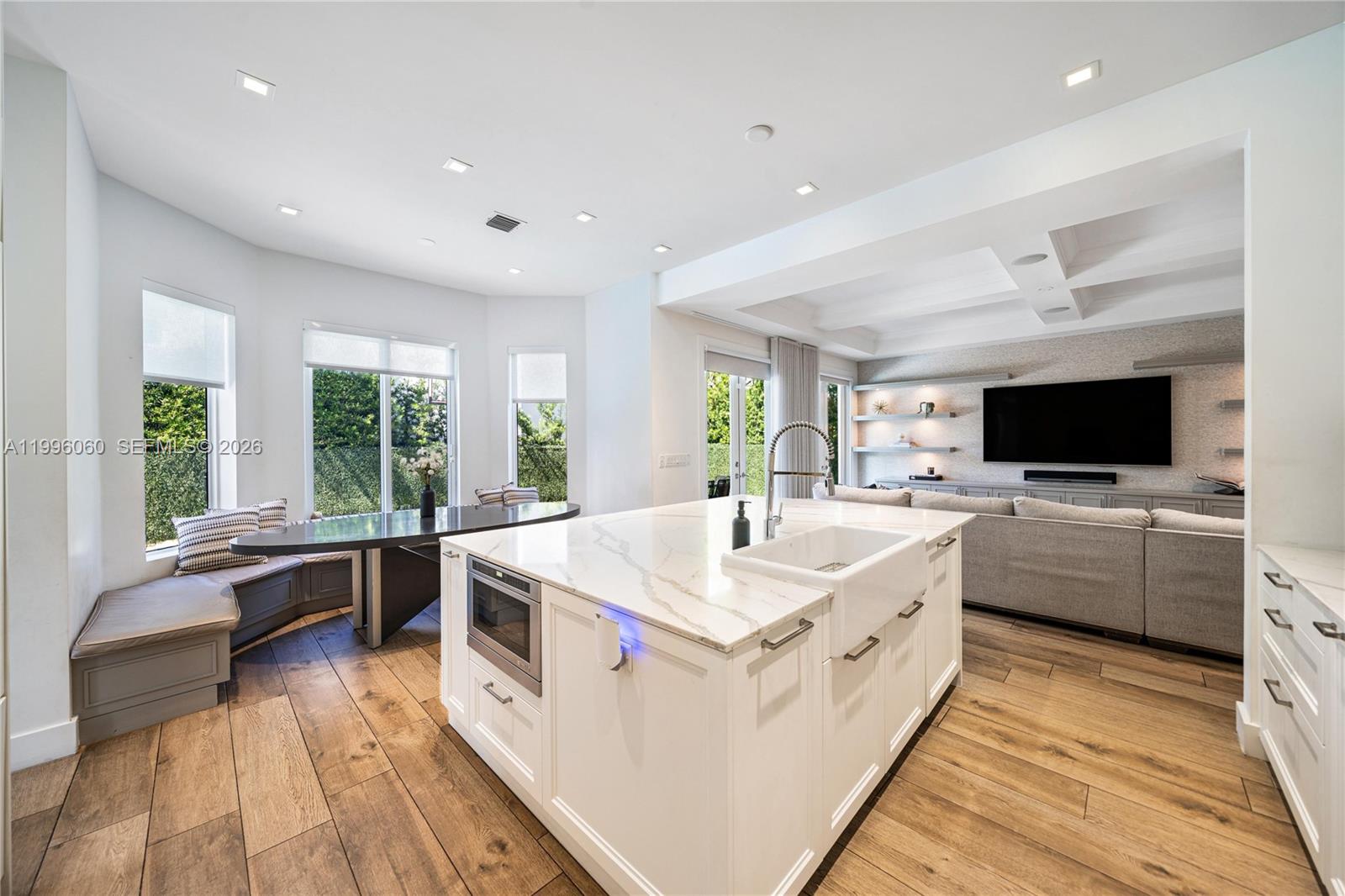 A modern white kitchen features a large marble-topped island, stainless steel appliances, and wood flooring — 3703 NE 199th St, Aventura FL 33180, AVENTURA, FL