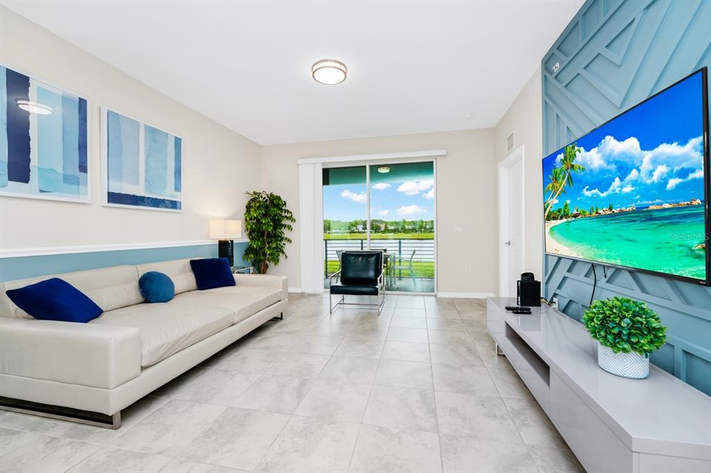 A living room features a white sofa, a television on a blue accent wall, and a balcony — 3171 PARADOX CIRCLE UNIT 104, KISSIMMEE, FL