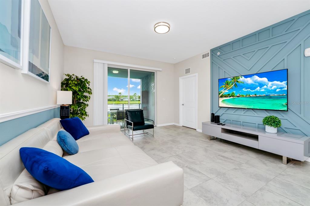 A living room features a blue accent wall with geometric molding, a television, and tile flooring — 3171 PARADOX CIRCLE UNIT 104, KISSIMMEE, FL