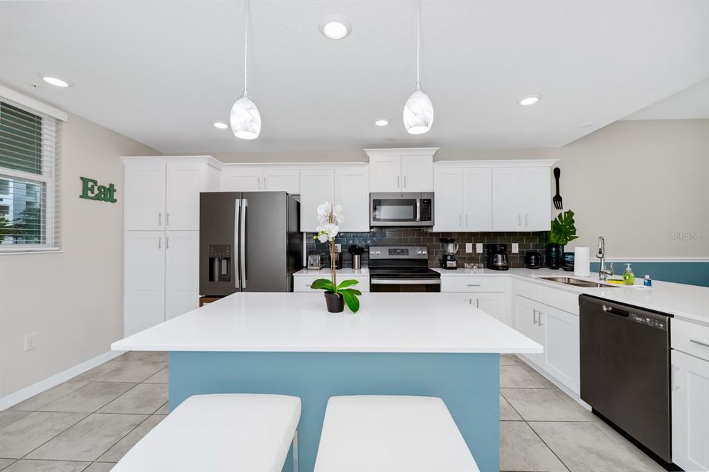 A kitchen features white cabinets, a blue island with seating, and stainless steel appliances — 3171 PARADOX CIRCLE UNIT 104, KISSIMMEE, FL