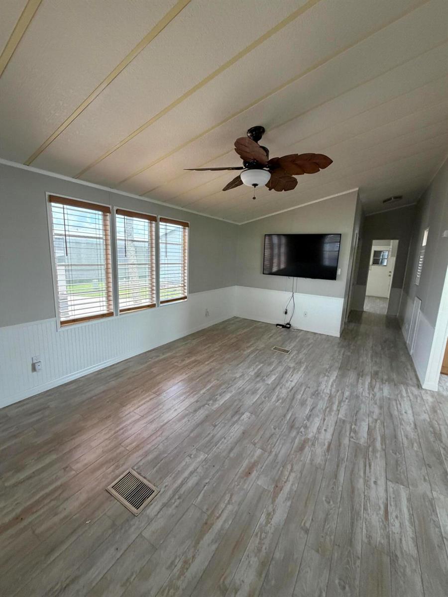 A living room with light wood-look flooring, white wainscoting, a ceiling fan, and a wall-mounted television — 5367 SE 66th Avenue, Okeechobee FL 34974, OKEECHOBEE, FL