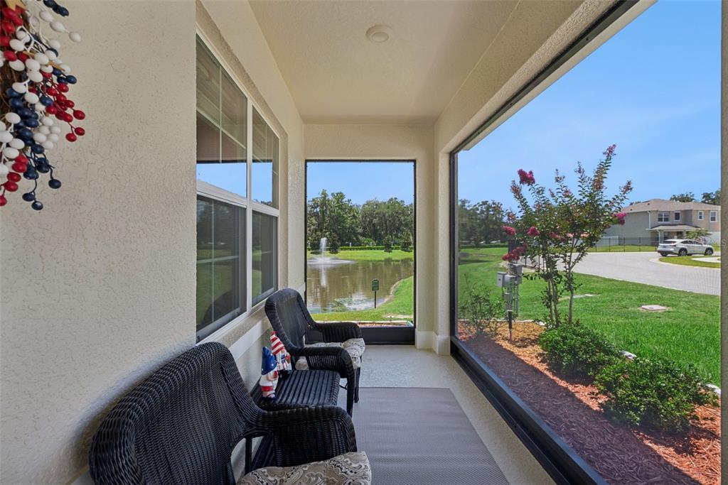 A screened-in porch features wicker furniture, a rug, and views of a pond and fountain — 4076 SAPSUCKER LOOP, SANFORD, FL