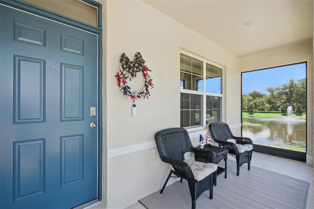A covered porch features a blue door, two wicker chairs, and a view of a pond — 4076 SAPSUCKER LOOP, SANFORD, FL