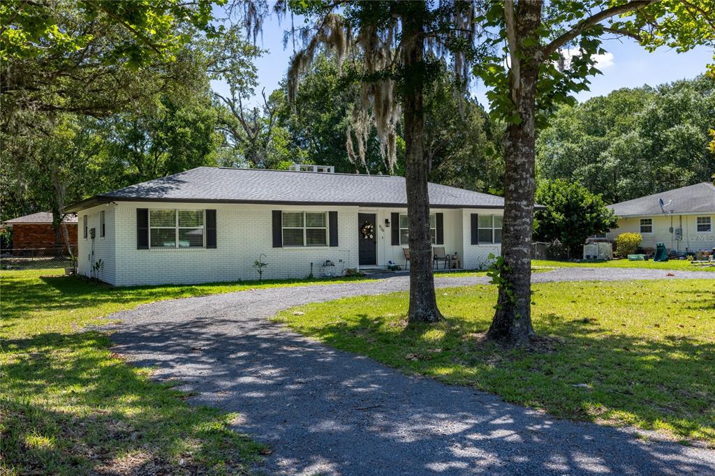 A single-story white brick house with a dark roof sits on a gravel driveway — 926 WOODLAWN STREET, STARKE, FL