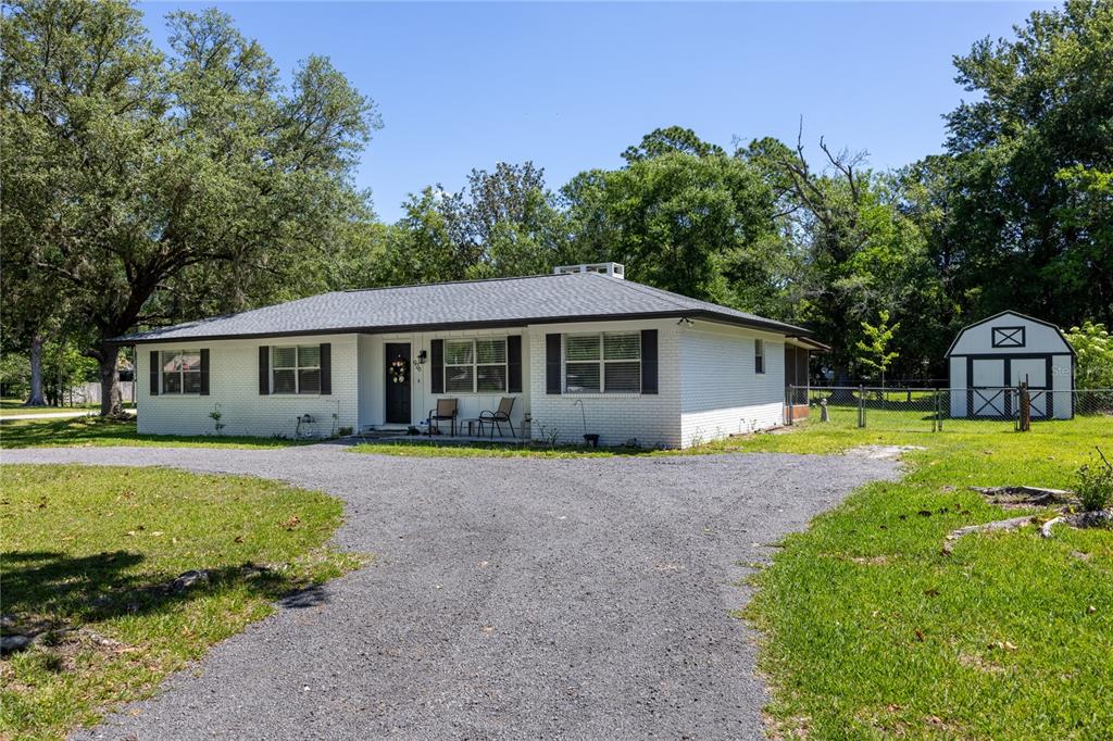 A single-story white brick house with a gravel driveway and a detached shed — 926 WOODLAWN STREET, STARKE, FL
