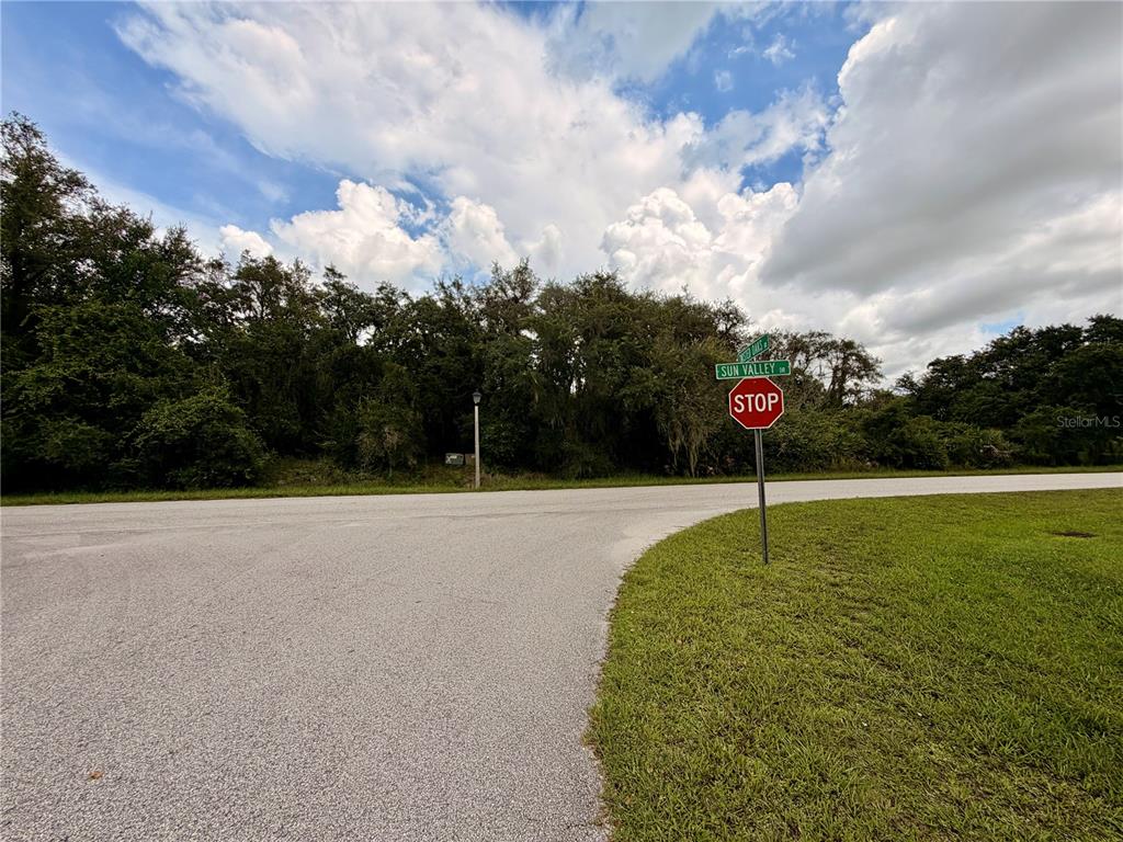 A stop sign stands at a street corner intersection bordered by trees and grass — 5709 SUN VALLEY DRIVE, SEBRING, FL
