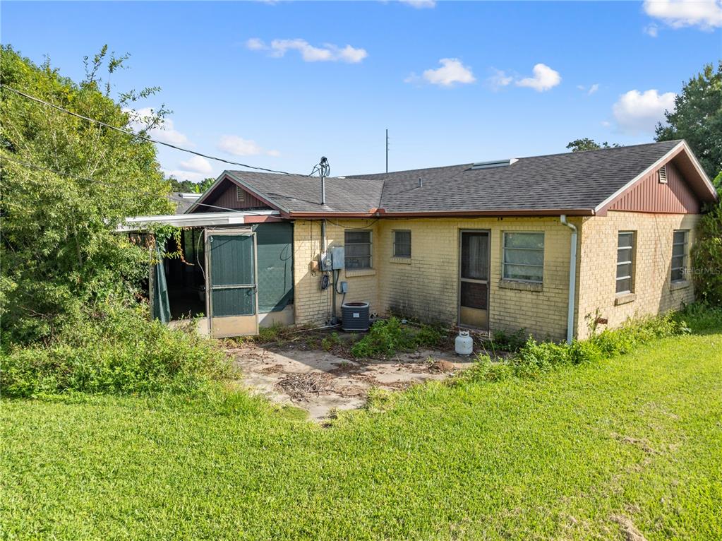 The exterior of a single-story yellow brick house with a screened porch and grassy yard — 740 SHORE DRIVE, KISSIMMEE, FL