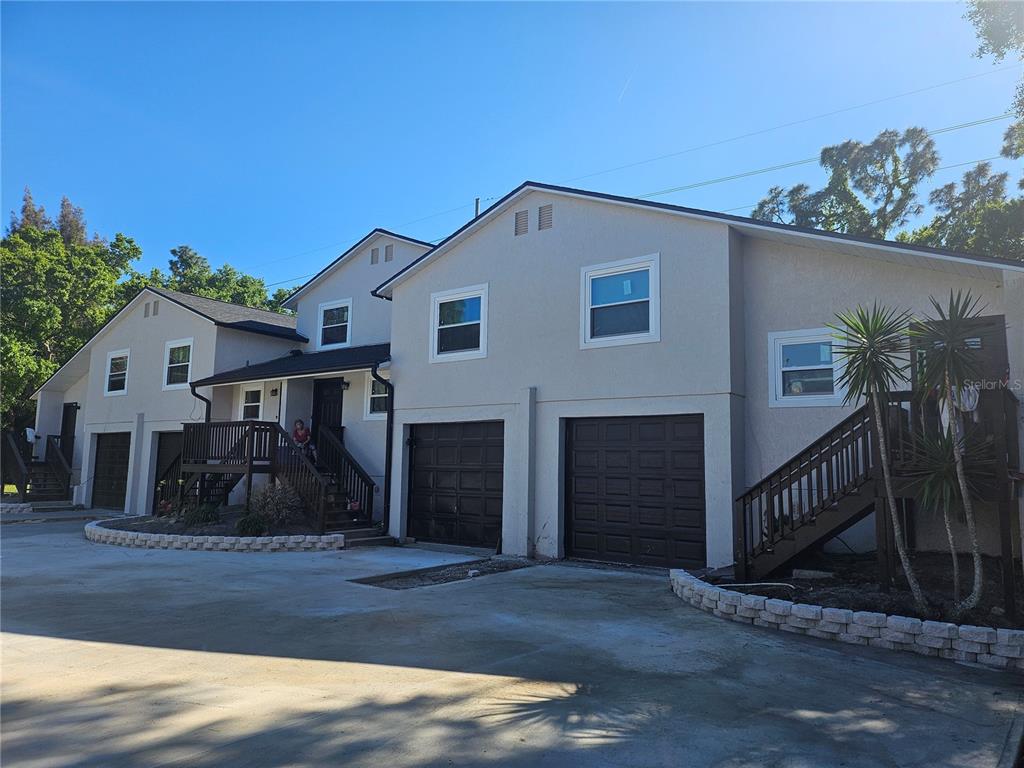 A multi-unit residential building with light-colored stucco, dark garage doors, and wooden staircases — 5802 MOHR LOOP UNIT 5802 5804 5806 5808, TAMPA, FL