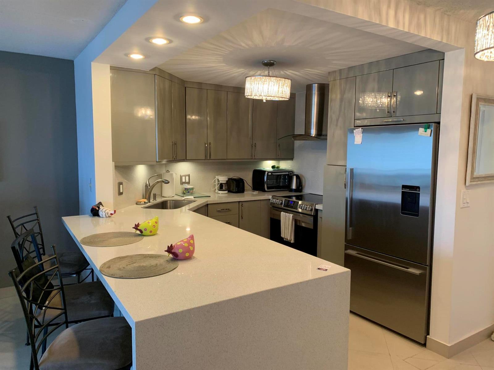 A modern kitchen features gray cabinets, stainless steel appliances, and a large white quartz island — 133 N Pompano Beach Boulevard # 808, Pompano Beach FL 33062, POMPANO BEACH, FL