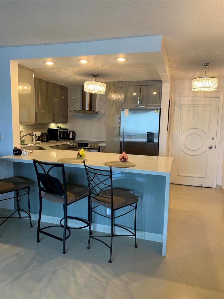 A modern kitchen features gray cabinets, stainless steel appliances, and a breakfast bar with stools — 133 N Pompano Beach Boulevard # 808, Pompano Beach FL 33062, POMPANO BEACH, FL