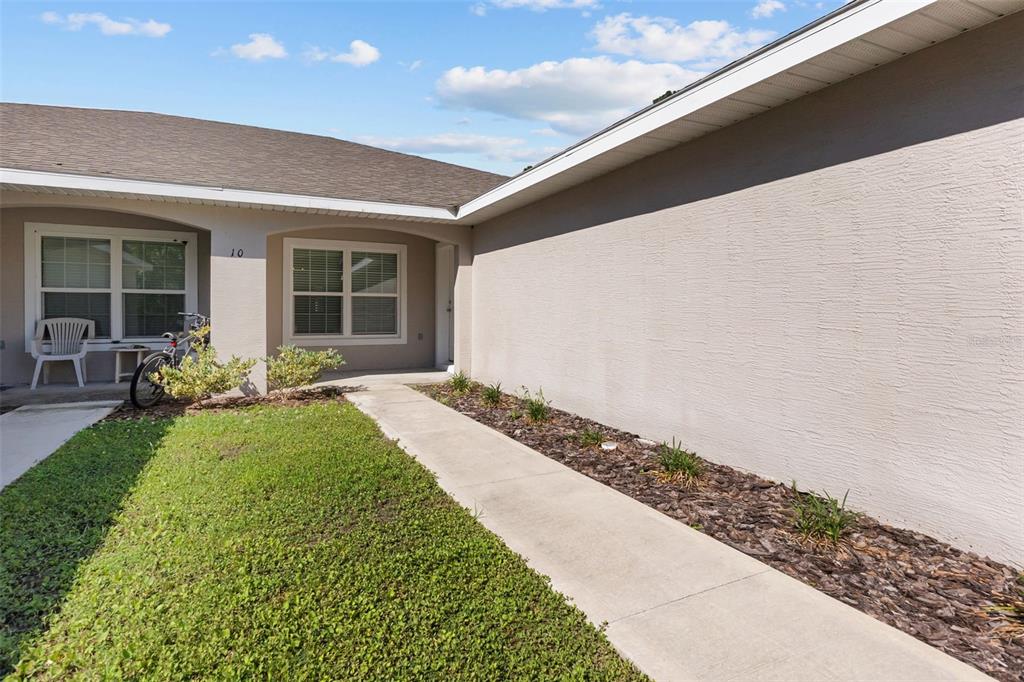 A concrete walkway leads to the front entrance of a house with beige stucco walls — 10 PONTIAC LANE, PALM COAST, FL