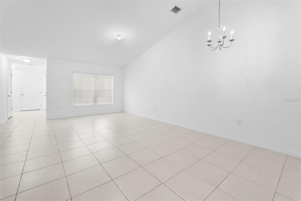 A bright, empty room features white walls, light-colored tile flooring, and a hanging chandelier — 10 PONTIAC LANE, PALM COAST, FL