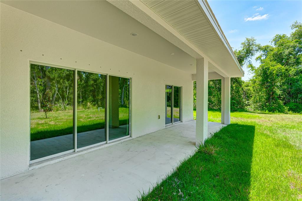 A concrete patio with sliding glass doors sits beneath a covered porch overlooking a yard — 3861 URIAH STREET, NORTH PORT, FL