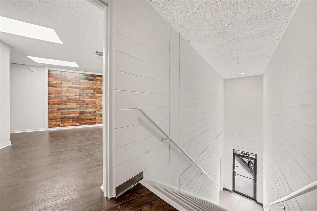 A staircase with white shiplap walls leads down to a glass door entrance — 4435 GUNN HIGHWAY, TAMPA, FL