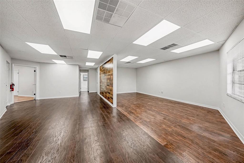 An empty office space features wood-look flooring, a wood-paneled accent wall, and drop ceiling lights — 4435 GUNN HIGHWAY, TAMPA, FL