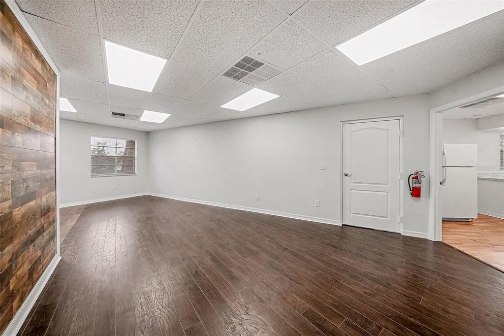An empty room features wood-look flooring, a wood-paneled accent wall, and a drop ceiling — 4435 GUNN HIGHWAY, TAMPA, FL