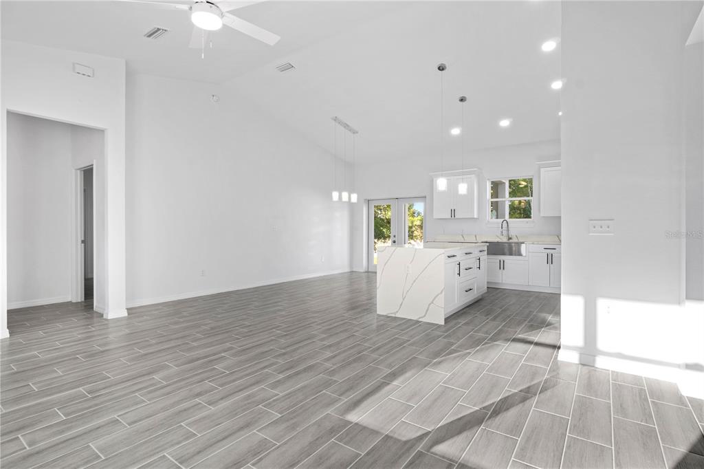 A bright, open-concept kitchen and living area features white cabinetry, a marble-topped island, and gray flooring — 42 JUNIPER PASS TERRACE, OCALA, FL