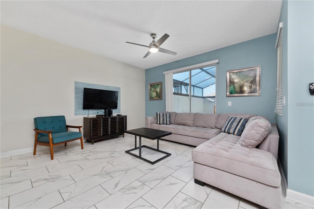 A living room features a gray sectional sofa, a teal armchair, and white marble-look tile flooring — 8930 STINGER DRIVE, DAVENPORT, FL