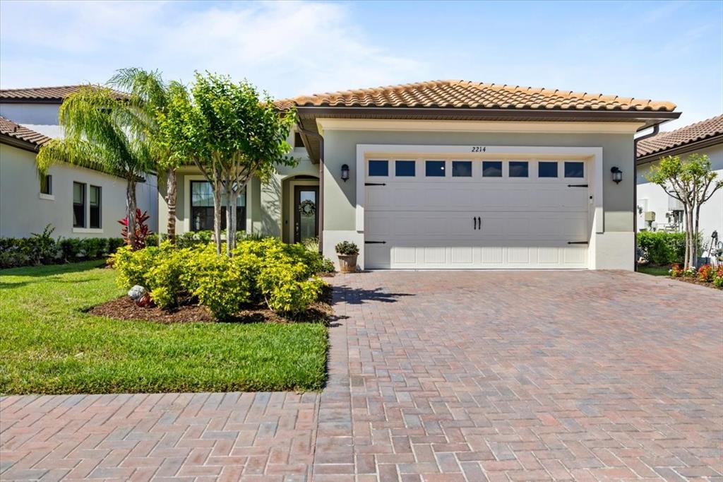 A single-story house with a beige stucco exterior, tile roof, and a brick paver driveway — 2214 5TH STREET E, PALMETTO, FL