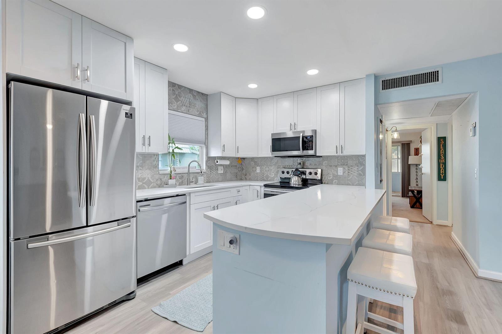 A kitchen with white cabinets, stainless steel appliances, a quartz island, and light blue walls — 89 Flanders Way # B, Delray Beach FL 33484, DELRAY BEACH, FL